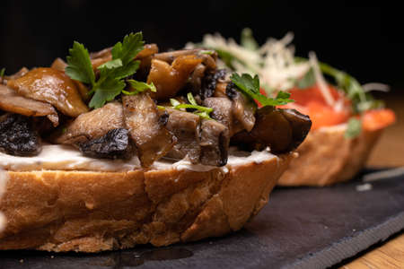 Bruschetta with mushrooms, soft cheese and herbs on a black background. Delicious sandwiches and...