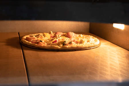Pizza is baked in the oven. The process of cooking Italian pizza, oven, high temperature. Pizza with chicken, tomatoes and cheeseの写真素材