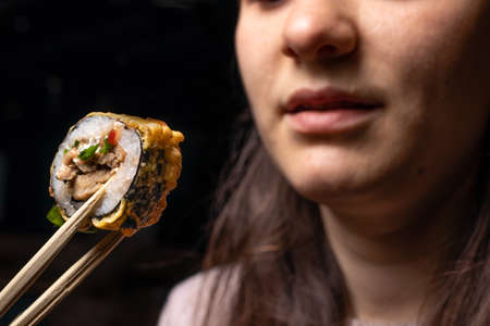 A woman holds a roll with wooden sticks for sushi. Sea food, raw fish, Japanese traditional cuisine.の写真素材