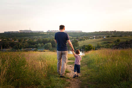 Dad and son walk in a yellow summer field in the evening at sunset and eat candy on a stick. Fathers Day, love in the family, the role of the father in raising the child.の写真素材