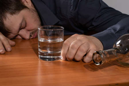 A man in alcoholic intoxication holds a glass of alcohol. Alcoholism, addiction, delirium.