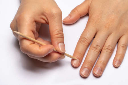 Female hand and orange stick. Cuticle retraction during manicure. Nail care at home.の写真素材