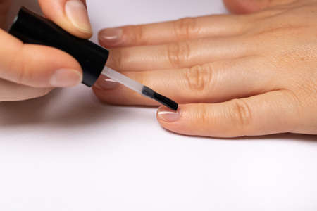 A woman covers her nails with a rubber base for gel polish. Manicure at home.の写真素材