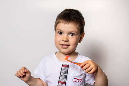 A little boy holds an orange toothbrush with toothpaste. The child brushes his teeth, prevention of tooth decayの写真素材