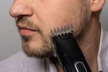 A man shaves his beard with a trimmer razor. Modeling beard, masculine style, facial hair care, morning routines in the bathroomの写真素材