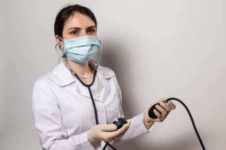 Doctor in a medical mask, cardiologist measures blood pressure with a blood pressure monitor.