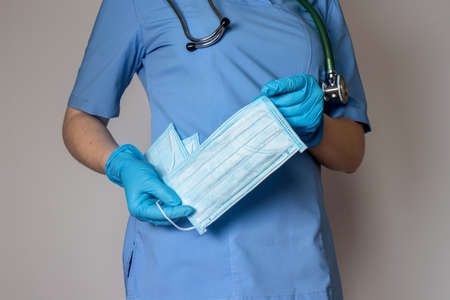 A doctor in a medical mask and blue uniform holds many medical protective masks.の写真素材