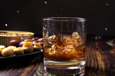 Whiskey with ice sprinkled from a glass. Snack for Whiskey: pickled mushrooms champignons, olives...