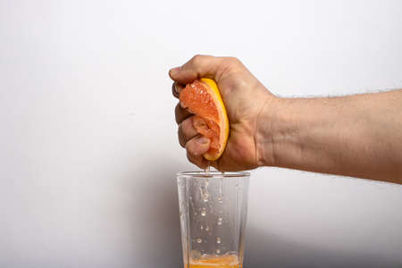 Male strong hand squeezes juice from a ripe grapefruit into a glass. Fruit citrus juice.の写真素材