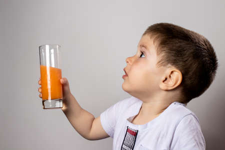 A little boy holds a glass of orange juice in his hands and smiles. Juices and vitamins in the diet...
