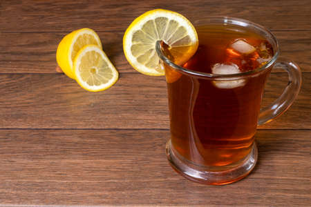 Black tea with lemon and ice in a transparent glass large mug on a brown wooden background.の写真素材