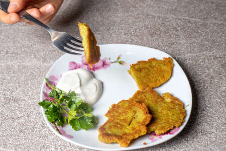 Potato pancakes on a plate, served with sour cream and parsley.