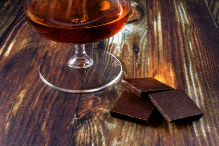 Glass with cognac and dark chocolate. Dear elite alcohol on a dark brown background. Alcoholic drinks.の写真素材