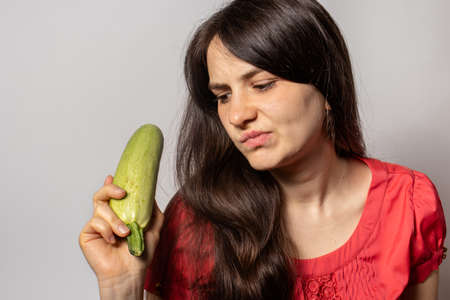 The girl holds zucchini in her hand and frowns displeasedly. Ketodiet, raw food diet, gluten-free...
