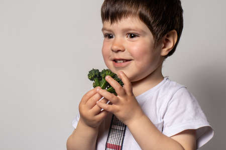 A little boy holds a green broccoli in his hands, sniffs it and smiles. Proper nutrition and healthy lifestyle for children. Vegetables in the diet of children.の写真素材