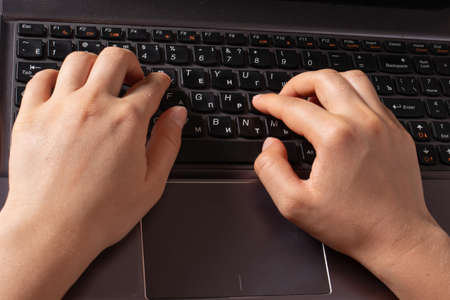 Human hands are typing text on a black laptop keyboard.