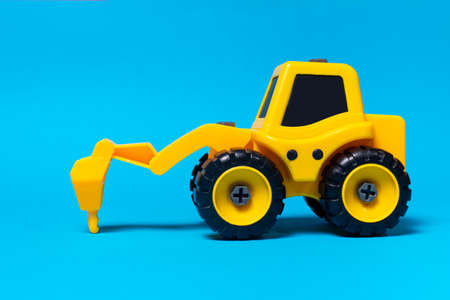 Childrens toy yellow tractor truck drill on a blue background. Plastic construction equipment, toy store.の写真素材