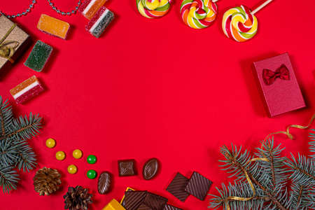 Candy, marmalade and chocolate on a red background with Christmas decoration, gifts, ribbons and spruce branches on a red background. Banner for a pastry shop with a place for text.の写真素材