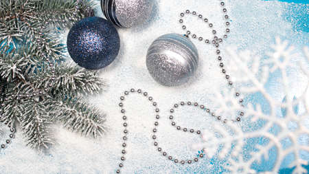 Spruce branch with Christmas toys and beads on a snow-covered white background. A holiday card,...