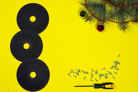 Cutting wheel for metal, screws and a screwdriver on a yellow background with a spruce branch. New year banner for hardware store and construction.の写真素材