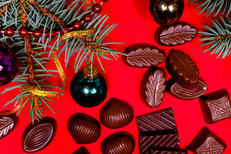 Pieces of chocolate and candy on a red New Years background with spruce branches and balls with a...
