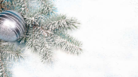 Spruce branch with Christmas toys and beads on a snow-covered white background. A holiday card,...