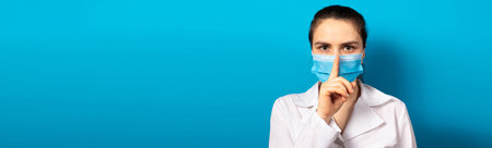 The doctor in the mask shows a sign of silence finger at the mouth. Medical mystery in medicine and health care, medical error and secrets of new medical research. Medical secrecy.の写真素材