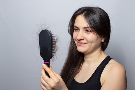 The girl is holding a hairbrush with her hair falling out and smiling. Hair loss, hair care and...