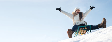 Woman sits and sledges from the mountain against the background of snow and sky in winter. Banner for ski resort.の写真素材