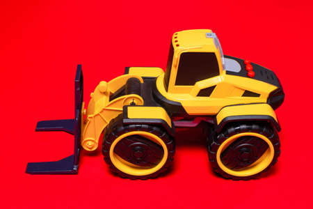 The yellow black forklift toy typewriter on a red background. Construction equipment tractor for...