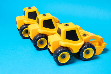 Three yellow tractors on a blue background, construction toys of a boy's car for a toy store.の写真素材