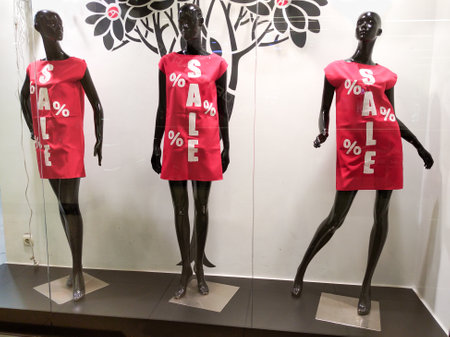 Three black mannequins in red dresses with the inscription Sale on the shop window. Buying and selling clothes for women.の写真素材