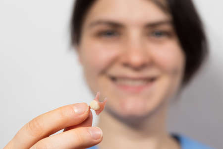 Dentist holding ceramic artificial false unit tooth. Dental prosthesis in gloved hands of the doctor close-up. Dentistry conceptual photo. Prosthetic dentistry. False teeth.の写真素材