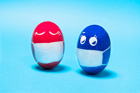 Two Masked Easter eggs on a blue background. The concept of a world-class  pandemic and quarantine during the Easter holidayの写真素材