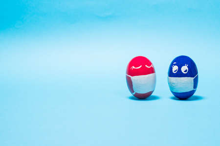 Easter eggs in protective masks on a blue background - the Easter holiday during the  epidemic and quarantine. Banner with place for text copy spaceの写真素材