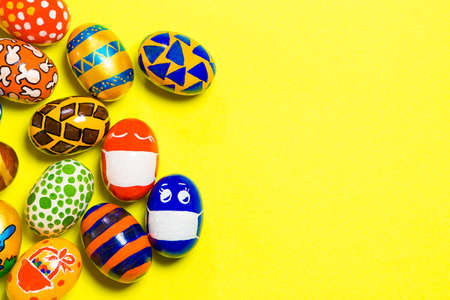 Colored colored eggs on a yellow background. Two eggs in a mask due to the quarantineの写真素材