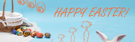 Beautiful Easter horizontal long banner with a basket of eggs and bunny ears with the inscription Happy Easter on a light minimalist blue background.の写真素材