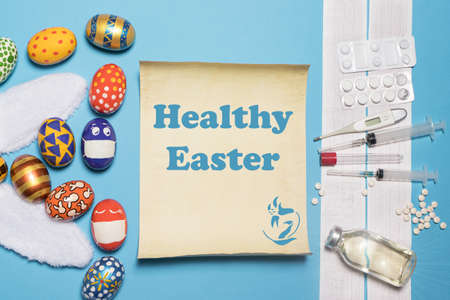 A medical banner with ECG, medicines and syringes with the Easter concept painted eggs and rabbit ears on a blue background with the inscription Healthy Easter.の写真素材