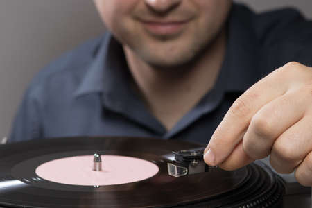 A man and vintage record player while recording, the record spins and music plays. Gramophone and...