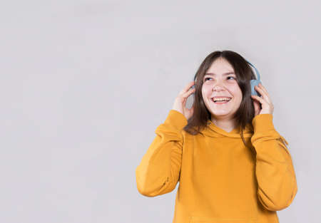 A teenage girl with long dark hair smiles and laughs in a bright orange hoodie in headphones with place for text and copy space.の写真素材