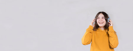 A teenage girl in a bright hooded sweatshirt on her head and headphones looks at the space for the text to the side. Learning online, schooling remotely. Banner na light backgroundの写真素材