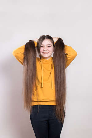 A 12-year-old teenage girl with very long natural hair smiles. Vertical photo with a place for text copy space. Children's hairdresser, haircut, hairstyles for long hair in children.の写真素材