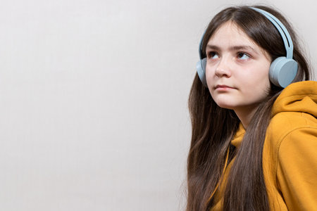 A sad teenage girl, 12-13 years old, sits in headphones sweatshirt on a white background copy space for text. Adolescent problems, loneliness, bullying at school.の写真素材