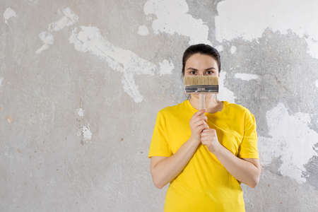 A woman repairman in a yellow bright t-shirt holds a brush. Place for text. Turnkey repairs.