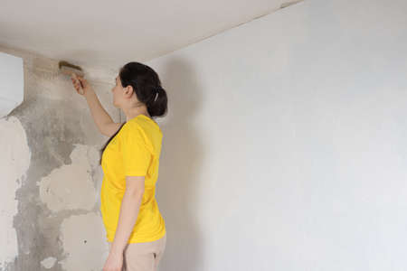Woman repairman smears the wall with glue. Sticking wallpaper in the house yourselfの写真素材