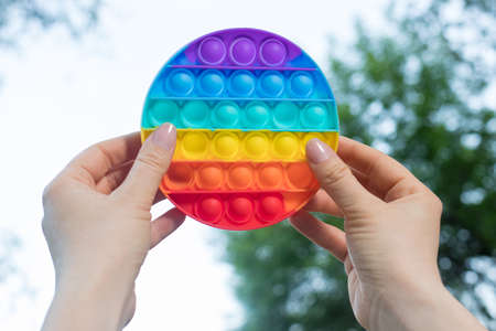 Colored trendy toy Pop it in the hands of an adult on the background of a sky in nature. Antistress...
