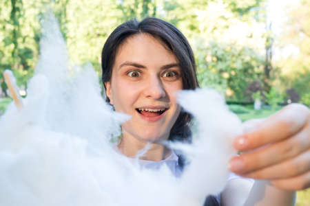 The brunette girl in admiration tears off a piece of cotton candy. Delight and happy eyes from sweet food, hot discounts in stores and a special offerの写真素材