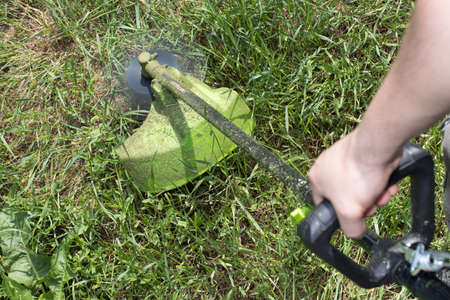 A man with an electric lawn mower mows the grass. For a gardening equipment store.