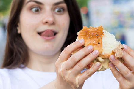 Brunette woman overeats on a burger on the street. Gluttony, excess calories, and bulimia.