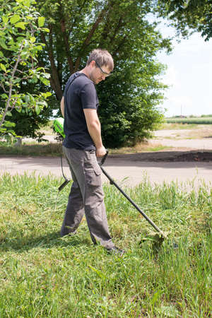 A man with an electric lawn mower mows the grass. For a gardening equipment store, vertical photo.